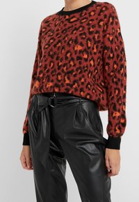 Rode en oranje leopardprint trui met een zwarte geribbelde halslijn en manchetten, gecombineerd met zwarte, hooggesneden leren broek.