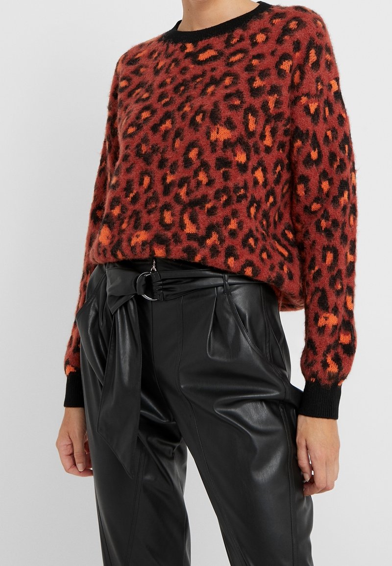 Rode en oranje leopardprint trui met een zwarte geribbelde halslijn en manchetten, gecombineerd met zwarte, hooggesneden leren broek.