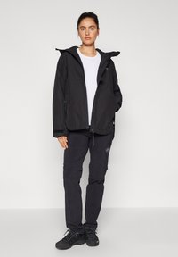Czarna wodoodporna kurtka z kapturem na białej koszuli, w połączeniu z czarnymi spodniami. Materiał jest gładki, o luźnym kroju i subtelnym oznakowaniu.
