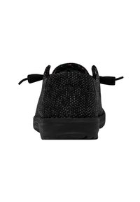 Zapatilla textil negra con superficie texturizada, suela negra plana y tiradores en el talón. Diseño minimalista con una forma aerodinámica.