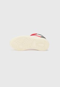 Semelle de sneaker en caoutchouc blanc cassé avec un motif de bande de roulement circulaire, présentant une sangle rouge et des accents noirs ; texturée pour une adhérence optimale.