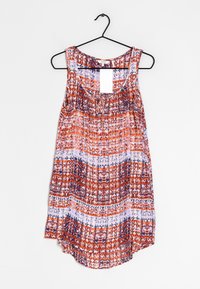 Ärmellose Damenbluse mit rot, weiß und blauem geometrischen Muster, Rundhalsausschnitt, hängt an einem schwarzen Kleiderbügel vor einem weißen Hintergrund.