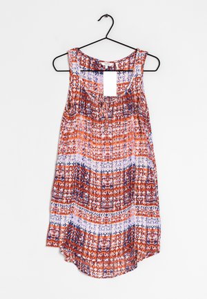 Top senza maniche da donna con motivi geometrici rosso, bianco e blu, scollo rotondo, appeso a una gruccia nera su uno sfondo bianco.