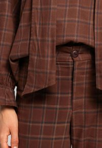 Tela de cuadro marrón con líneas rojizas y azul oscuro en unos pantalones con botón y una blusa de manga larga a juego con mangas con puños.