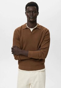 Suéter marrón de punto acanalado con cuello de polo, que presenta un escote en V y mangas largas, combinado con pantalones de un color claro. Diseño simple y texturizado.