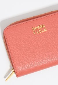 Cartera de cuero texturizado color coral con cremallera dorada y logotipo grabado "BIMBA Y LOLA" en la parte frontal. Acentos de hardware dorado.