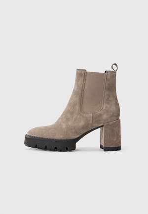 Botte cheville en daim taupe avec panneau latéral élastique, semelle crantée noire épaisse, talon bloc et tirette à l'arrière.