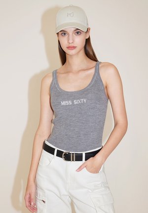 Šedý žebrovaný top s logem "MISS SIXTY", kombinovaný s bílými cargo kalhotami a světle béžovou čepicí. Černý opasek se stříbrnou sponou jako akcent.