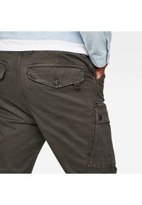 Vihreät cargo-housut, joissa on useita taskuja, nappikiinnitys ja pehmeä, teksturoitu kangas. Näkyvät saumat ja rento leikkaus.