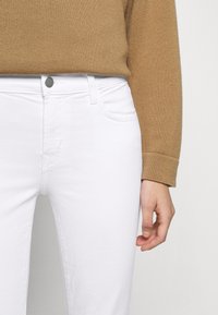 Jeans de mezclilla blanca con un ajuste clásico, que cuentan con bolsillos frontales, un cierre de botón metálico y detalles de costura sutiles. Combinados con un suéter beige.