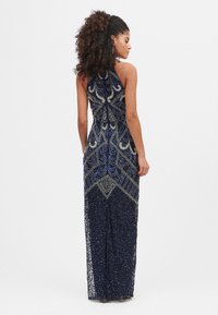 Podlahová námořnická modrá róba s propracovaným zdobením a vzory přilepených kamínků ve stříbrné a modré barvě. Má vykrojený výstřih a přiléhavý střih.