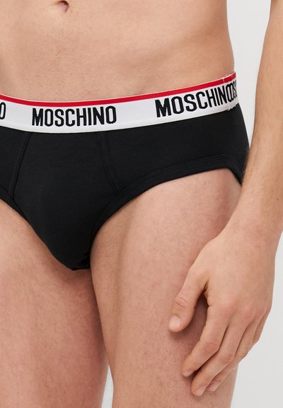 Culotte en coton noir avec une taille blanche arborant le texte "MOSCHINO" en rouge et noir. Texture lisse et design ajusté.