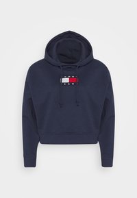 Marinblå huvtröja med kortad design, försedd med en central logotyp i rött, vitt och blått. Inkluderar dragsn ören och ribbade mudd.