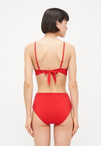 Rødt bikini sæt med en bandeau top med justerbare stropper og snørelukning bagpå, parret med højtaljede bunddele, glat tekstur, minimalistisk design.
