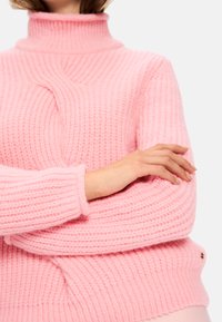 Rosa gestrickter Pullover mit hohem Kragen, gerippter Textur und weichem Finish. Verfügt über ein detailliertes Stickmuster und einen kleinen Logoakzent.