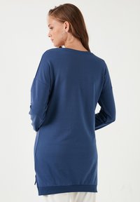 Dlouhá tunika z materiálu v námořnické modři, která má volný střih, zaoblený lem a postranní rozparky pro snadný pohyb. Hladká, lehká textura.