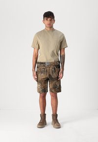 Beige Baumwoll-T-Shirt, braune Lederkurze mit dekorativen Nähten, silberner Schnallen-Gürtel und beige hohen Stiefel.