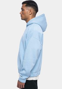 Light blue hooded sweatshirt with a relaxed fit, featuring a kangaroo pocket, ribbed cuffs, and a small logo on the chest.