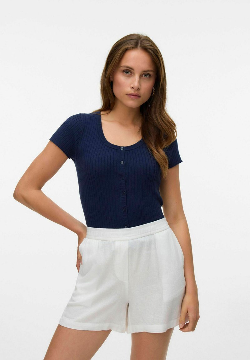 Tumši zils ribots t-krekls ar īsām piedurknēm un apaļu dekoltē, ar pogu detaļām, apvienots ar baltām lina šortiem, kas aprīkoti ar elastīgu jostu.