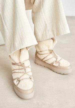 Bottes d'hiver beige doublées en shearling avec des lacets beige portées avec un pantalon large texturé crème.