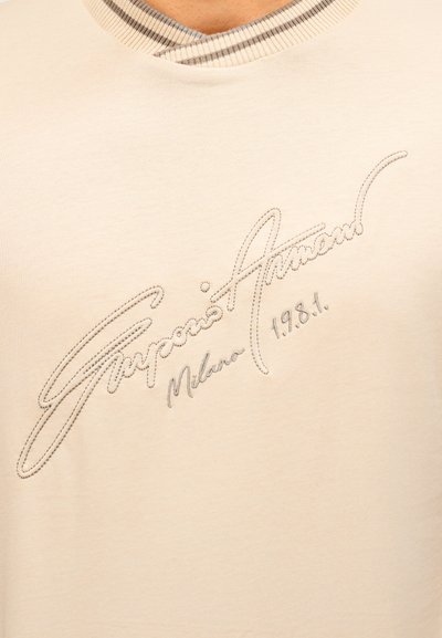 Μπεζ πουκάμισο με rib λαιμόκοψη και κεντημένο κείμενο στο στήθος που γράφει "Emporio Armani Milano 1981".
