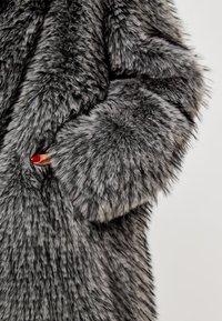 Tekstureret grå pelsfrakke med en blød, luksuriøs finish. Den har en bred manchet og en dyb lomme på siden, der fremhæver tydelige pelsmønstre.