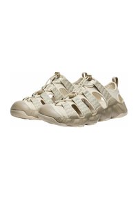 Sandali sportivi beige con tomaia in mesh traspirante, lacci elastici e suola in gomma robusta con un evidente motivo di battistrada.