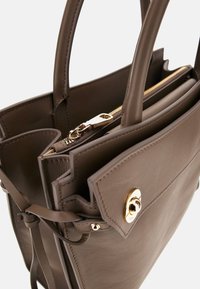 Borsa a mano in pelle marrone con due manici, chiusura con zip, accessoristica in oro e tasca esterna. Caratterizzata da una texture liscia e un design strutturato.