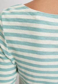 Primer plano de una persona que lleva una camisa de rayas horizontales en azul claro y blanco, mostrando la parte trasera y el área del hombro.