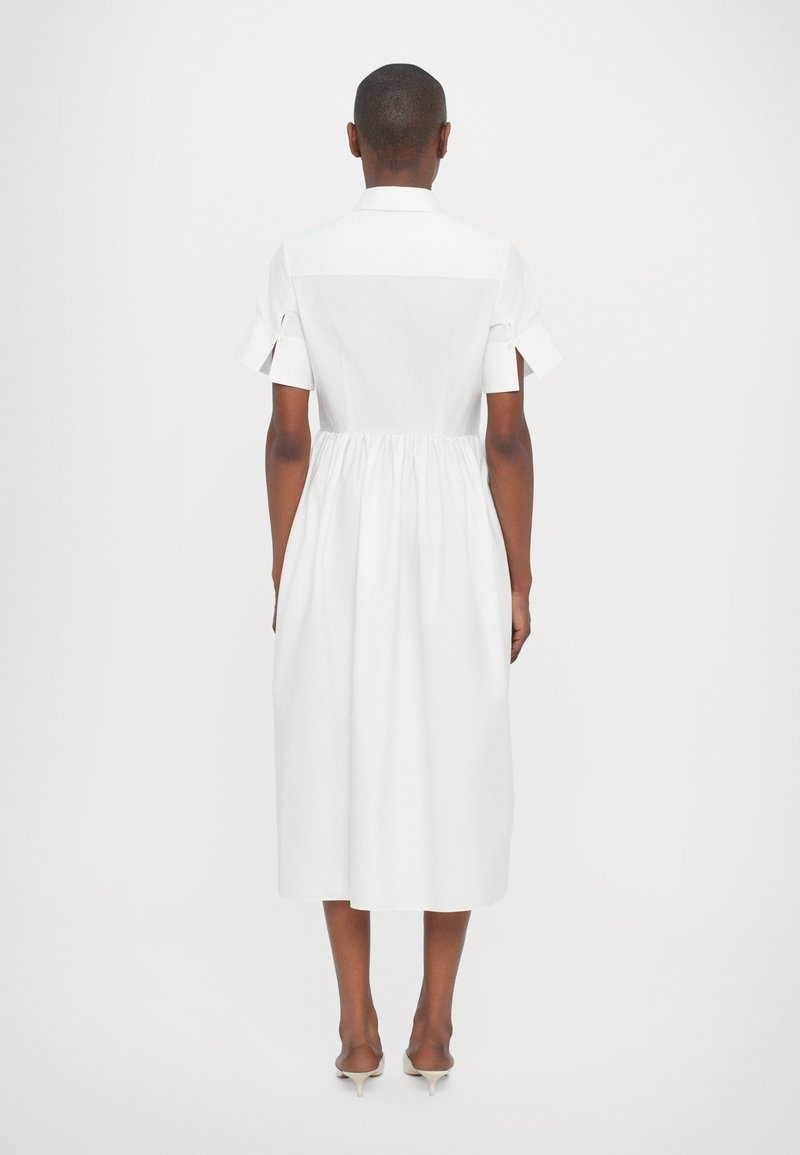 Abito bianco con maniche corte, corpetto aderente e vita arricciata. Presenta un colletto e un orlo fino al ginocchio, realizzato in tessuto morbido.