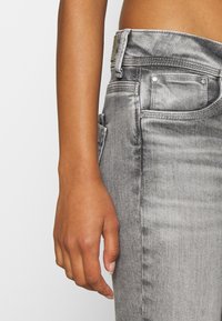 Jeans de mezclilla gris con un corte ajustado, que presentan una cintura alta, cinco bolsillos y detalles en metal plateado. Tejido texturizado con detalles de desgastado.