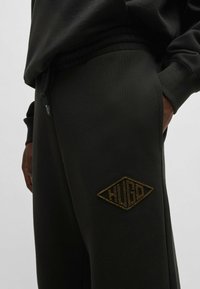 Sorte sweatpants med elastisk talje og lommer, med et diamantformet, guldbroderet "HUGO" logo på venstre lår.