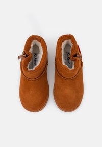 Botas de tobillo de ante marrón con un suave forro de piel blanca, que presentan un detalle decorativo trenzado en el cuello y una cremallera lateral.