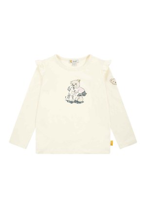 Long-sleeve cream shirt with ruffled shoulder accents. Features a printed bear and dog design. Includes a bear patch on the sleeve.
