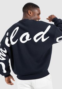 Sudadera de talle grande en azul marino, fabricada en algodón, con un gran texto blanco en la parte posterior, puños y dobladillo acanalados para un acabado ajustado.