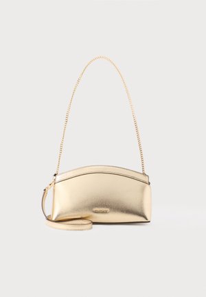 Malá metalická zlatá kabelka s oblou hranou nahoře, zlatým řetízkovým ramenním popruhem a odnímatelným náramkovým poutkem na bílém pozadí.