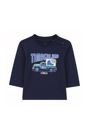 Marineblaues Langarmshirt mit einem Grafikdesign eines Vintage-Trucks und dem Schriftzug "TIMBERLAND" in Blau und Grün. Weiches Baumwollmaterial mit Druckknopfverschluss.