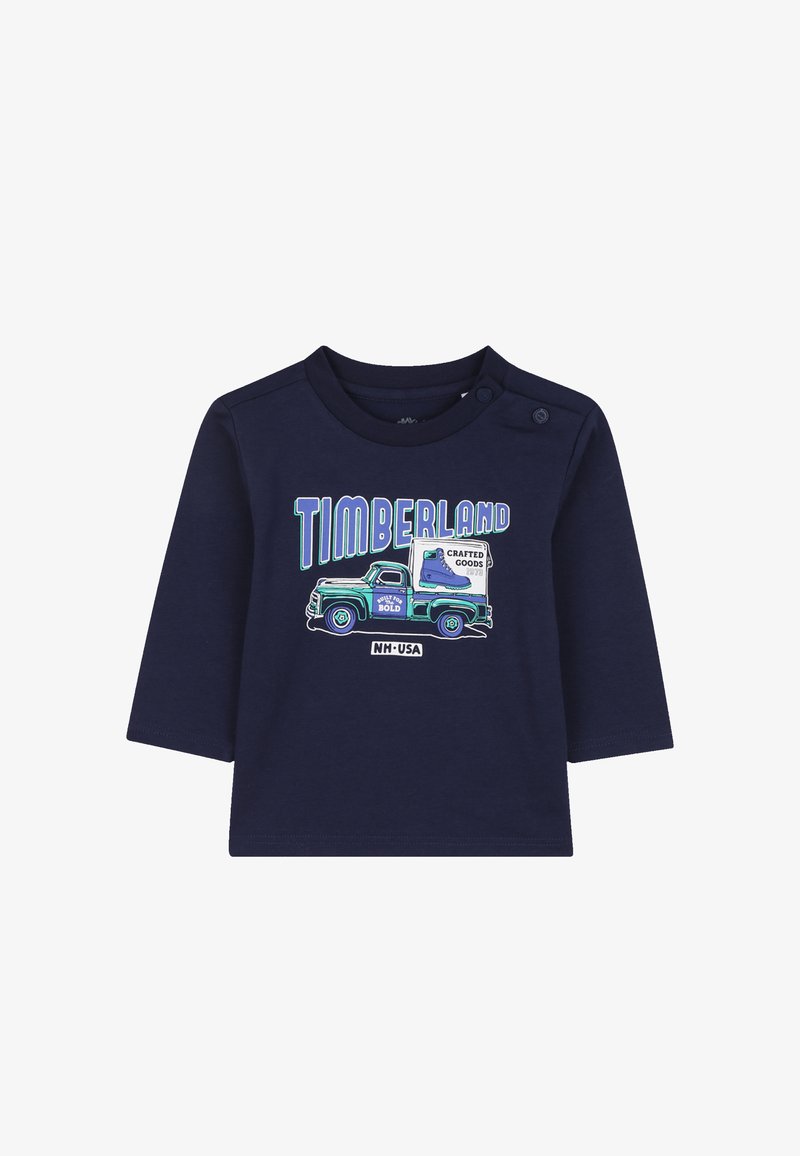Marineblauwe longsleeve shirt met een afbeelding van een vintage vrachtwagen en de tekst "TIMBERLAND" in blauw en groen. Zacht katoenen materiaal met drukknoopsluitingen.