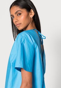 Vestido azul brilhante de mangas curtas com um corte solto, apresentando um laço nas costas e um design de costas abertas, feito de tecido leve.