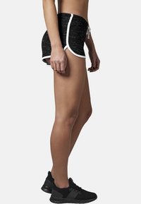 Černé sportovní šortky s texturovaným vzorem, bílým lemem a nastavovací šňůrkou. Nosené s černými teniskami. Boční pohled.