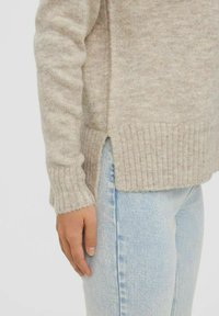 Beige, fuzzy knit sweater with ribbed cuffs and hem, featuring side slits for ease of movement. Paired with light blue denim.