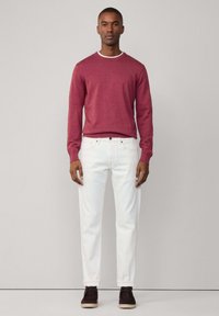 Pull à manches longues rouge avec col blanc, associé à un jean blanc. Le modèle porte des chaussures marron foncé avec une semelle claire. Design minimaliste.