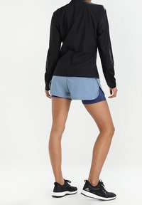 Veste noire à manches longues, short bleu clair et marine, chaussures de sport noires ; conçue pour le port actif avec une coupe épurée et fonctionnelle.