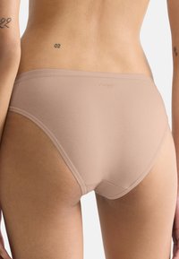 Beige puuvillaiset alushousut, joissa on sileä kangas, mid-rise-leikkaus ja minimalistinen muotoilu. Hieman näkyvä logo vyötäröllä.