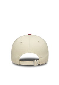 Beige színű baseball sapka piros felső gombbal; hátul anyagszíjjal rendelkezik, amelyen fém állító található a méret beállításához.