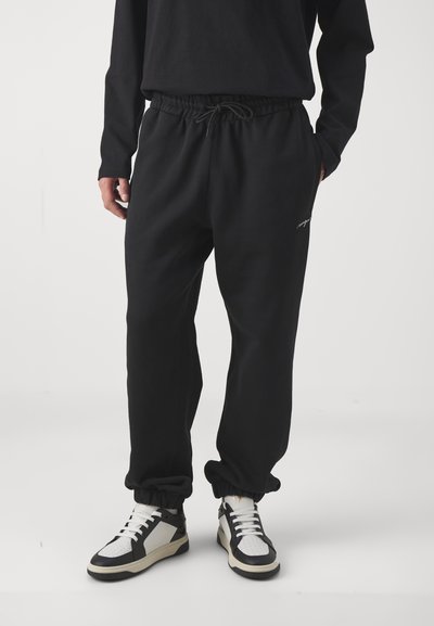 Sorte bomulds sweatpants med elastisk talje og manchetter, udstyret med et enkelt logodetalje på siden og sidelommer.