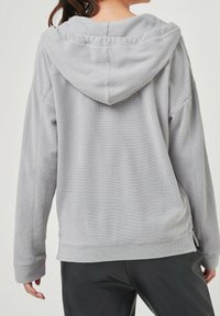 Světlě šedá mikina s kapucí z texturované látky, volný střih a žebrované manžety, s kapsou kangaroo a bočními rozparky na lemu.