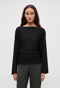 Must pikkade varrukatega topp, millel on lai kaelus ja vöökoha peal kogutud detailid. Sobitub mustade ja valgete triibuliste laiade pükstega.