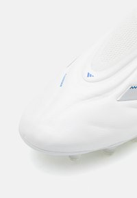 Weiße Fußballschuhe mit texturiertem synthetischem Obermaterial, das blaue Akzente und eine aerodynamische Form aufweist. Transparente Noppen an der Sohle für besseren Halt.