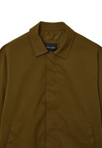Veste vert olive au design moderne, avec une fermeture avant sans boutons, deux poches latérales et un col classique. Le matériau est lisse et léger.
